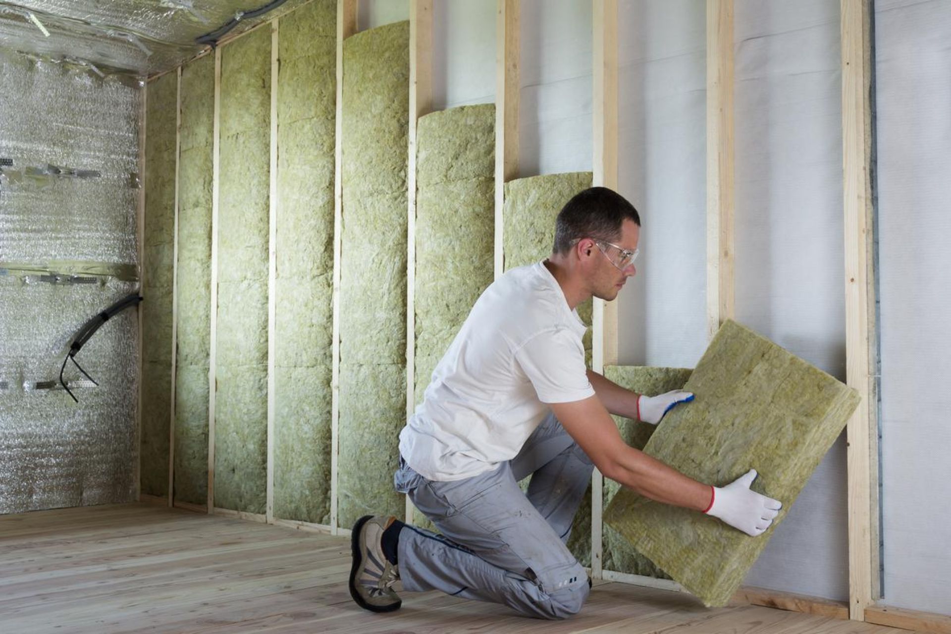A man installs insulation in a room, carefully placing material between the wall studs for energy efficiency.