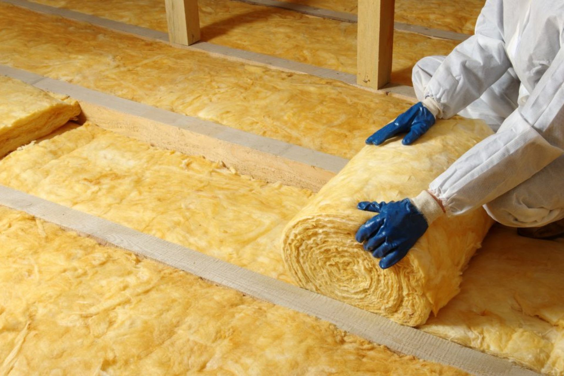A man in a white coat and gloves is installing floor insulation, showcasing his expertise in home energy efficiency improvements.