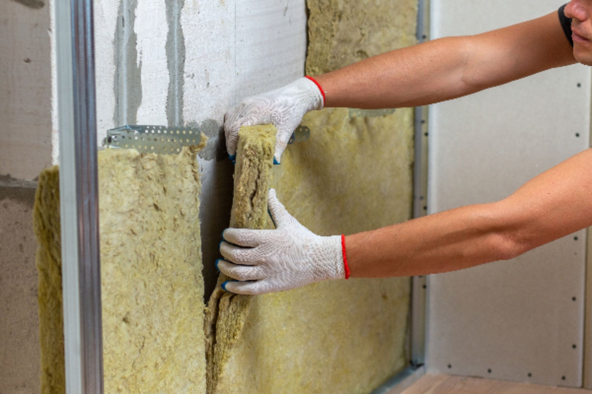 A worker in gloves installs insulation material into a wall frame, enhancing soundproofing and energy efficiency.
