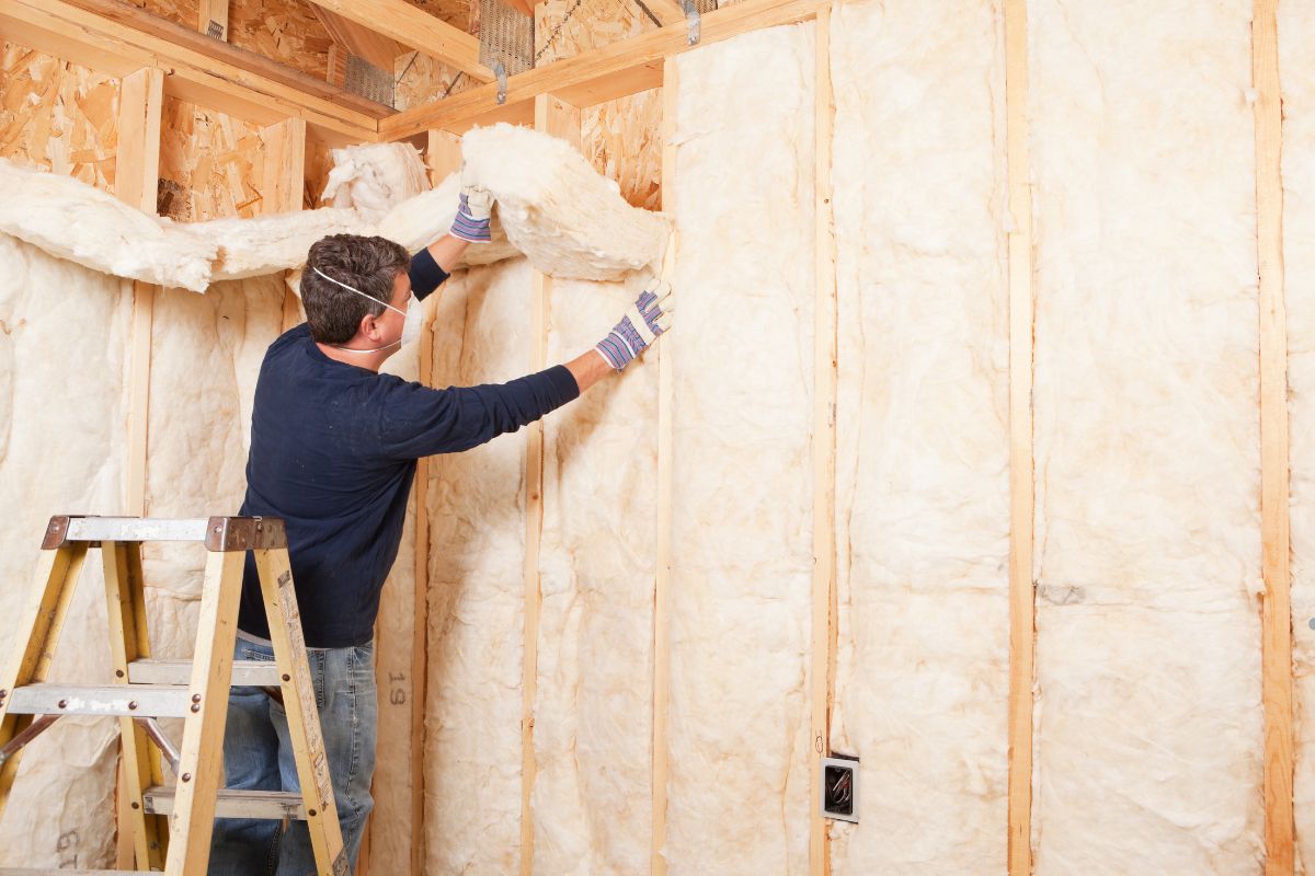  A man installs insulation in a room, demonstrating the process of improving energy efficiency. Call Insulation Professionals.