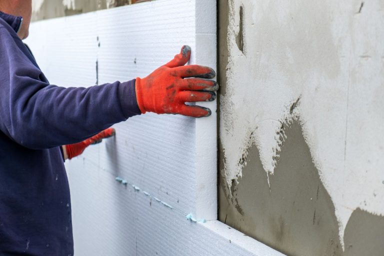 A man applies cement to a wall as part of the process to install insulation in interior walls.